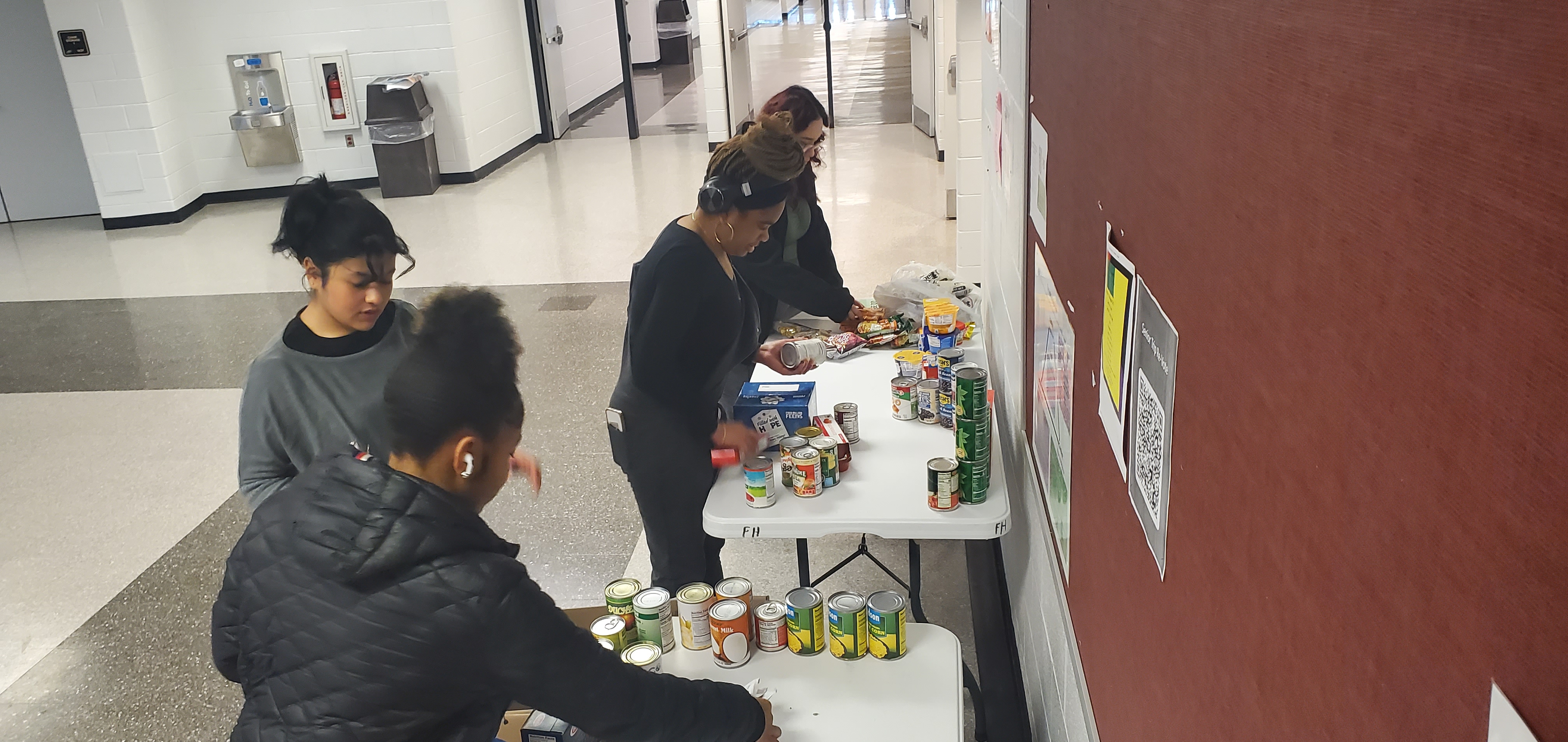students standing in front of a white table filled with canned food